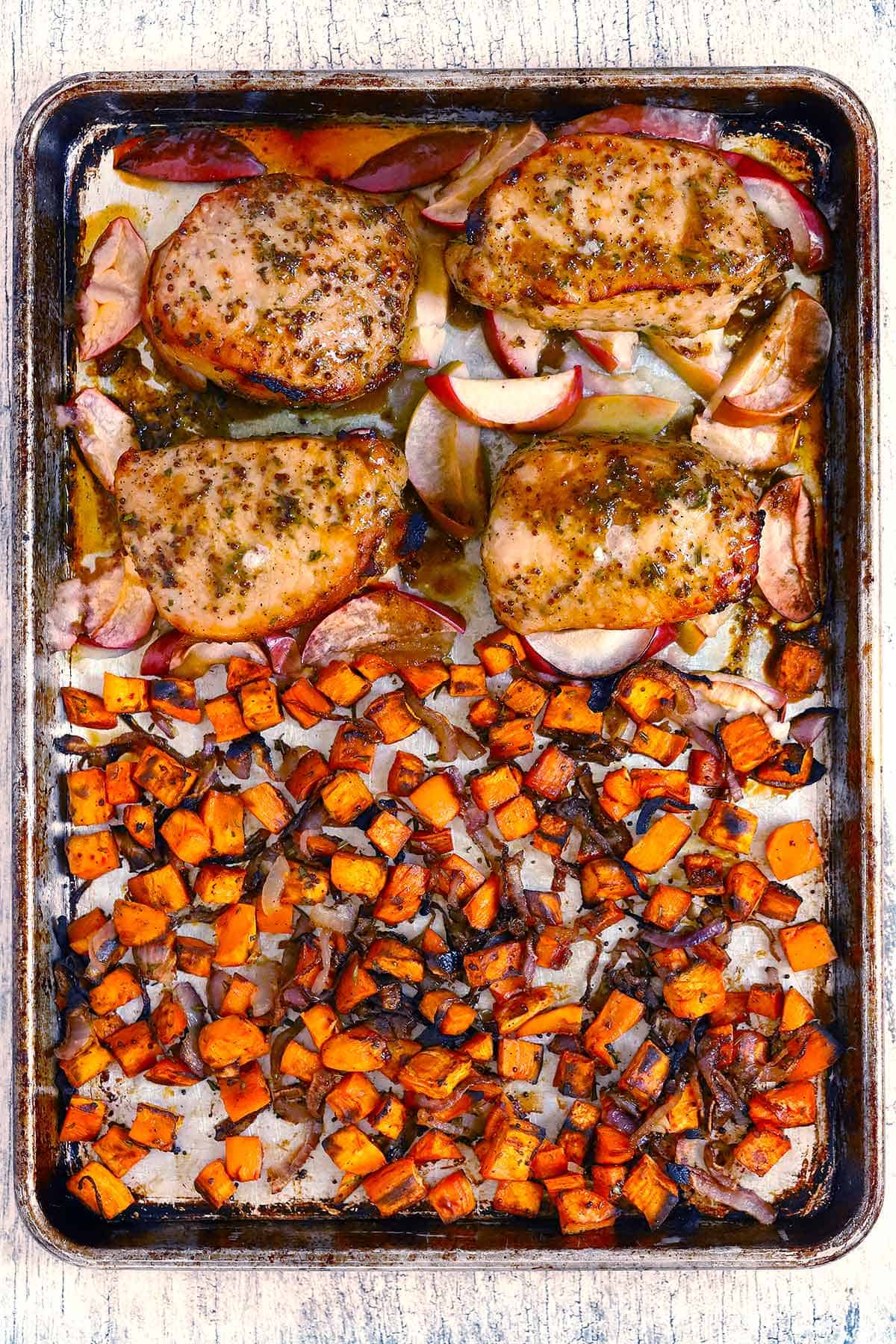 Sheet pan pork chops with apples and sweet potatoes on half bakers sheet with mustard rosemary maple dressing.
