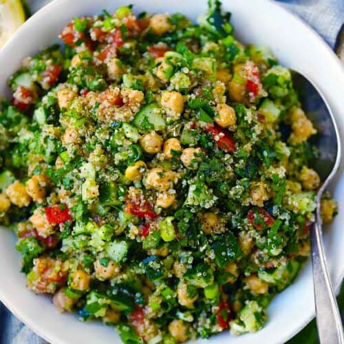 Square photo of quinoa chickpea tabbouleh salad with a serving spoon in a white bowl.