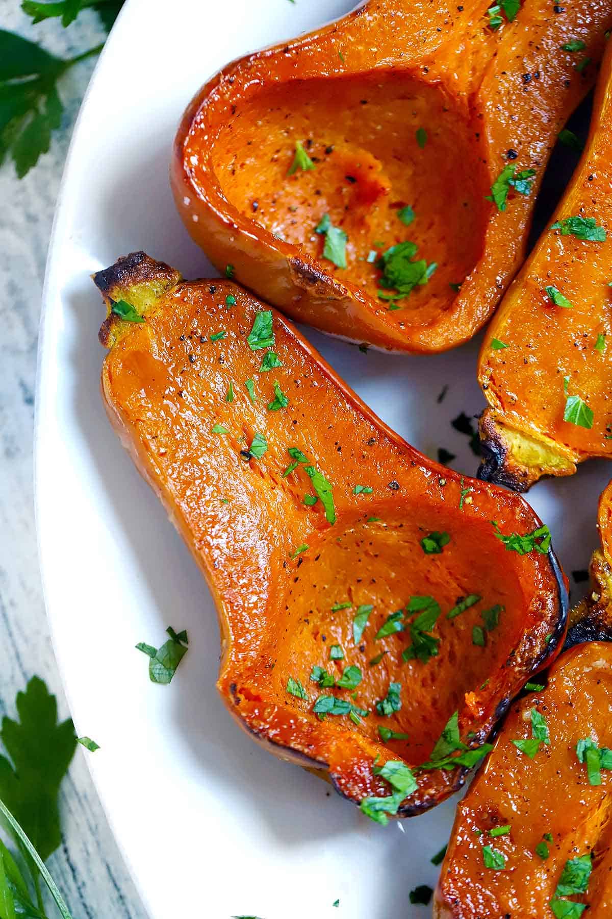 Close up photo of a roasted honeynut squash cut in half with herbs on top.