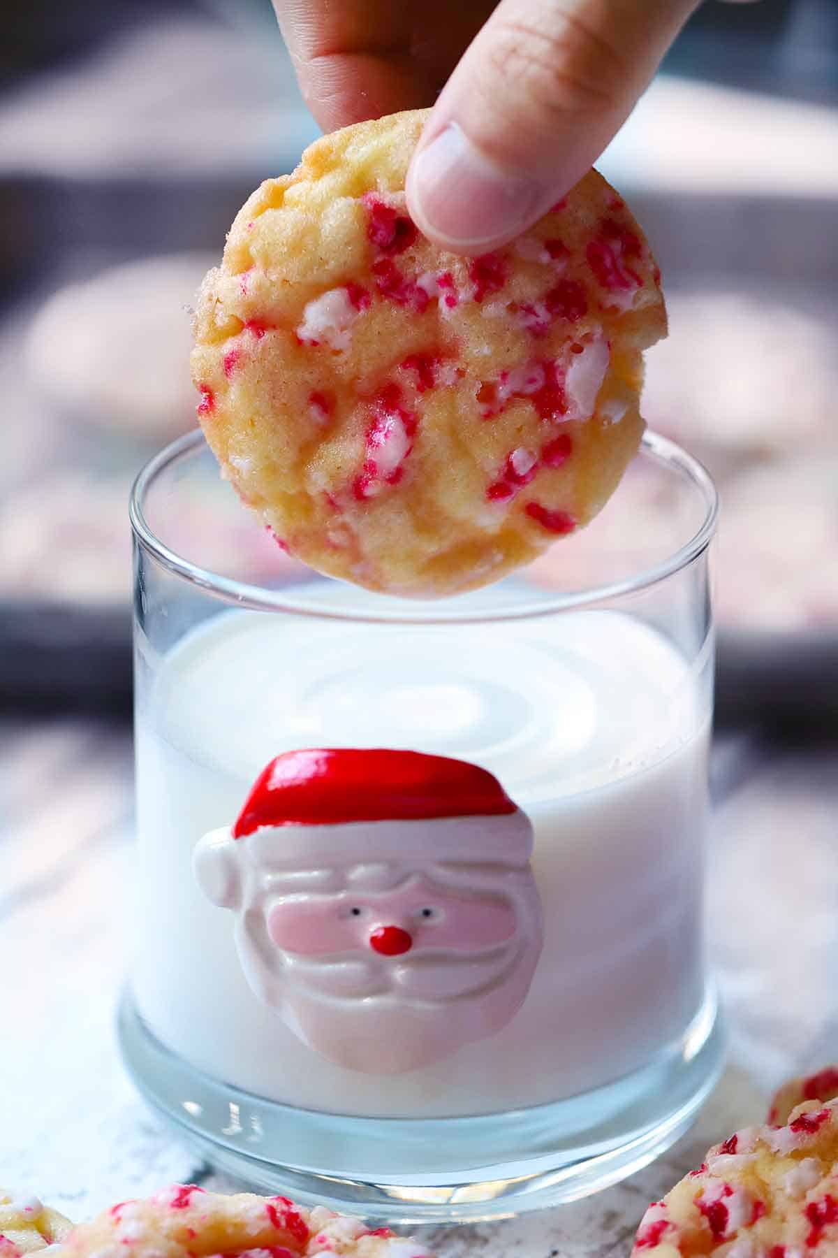 A peppermint cookie being dipped into a santa glass with milk in it.