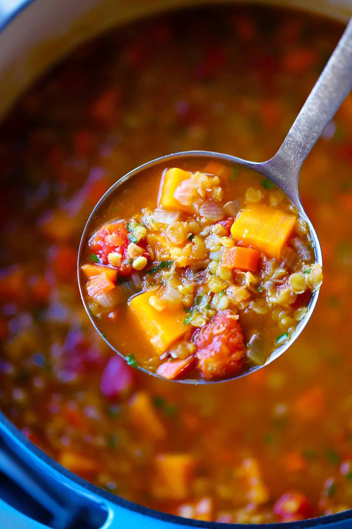 A ladleful of red lentil soup over a blue dutch oven.