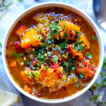 Square photo of red lentil soup with veggies topped with herbs.