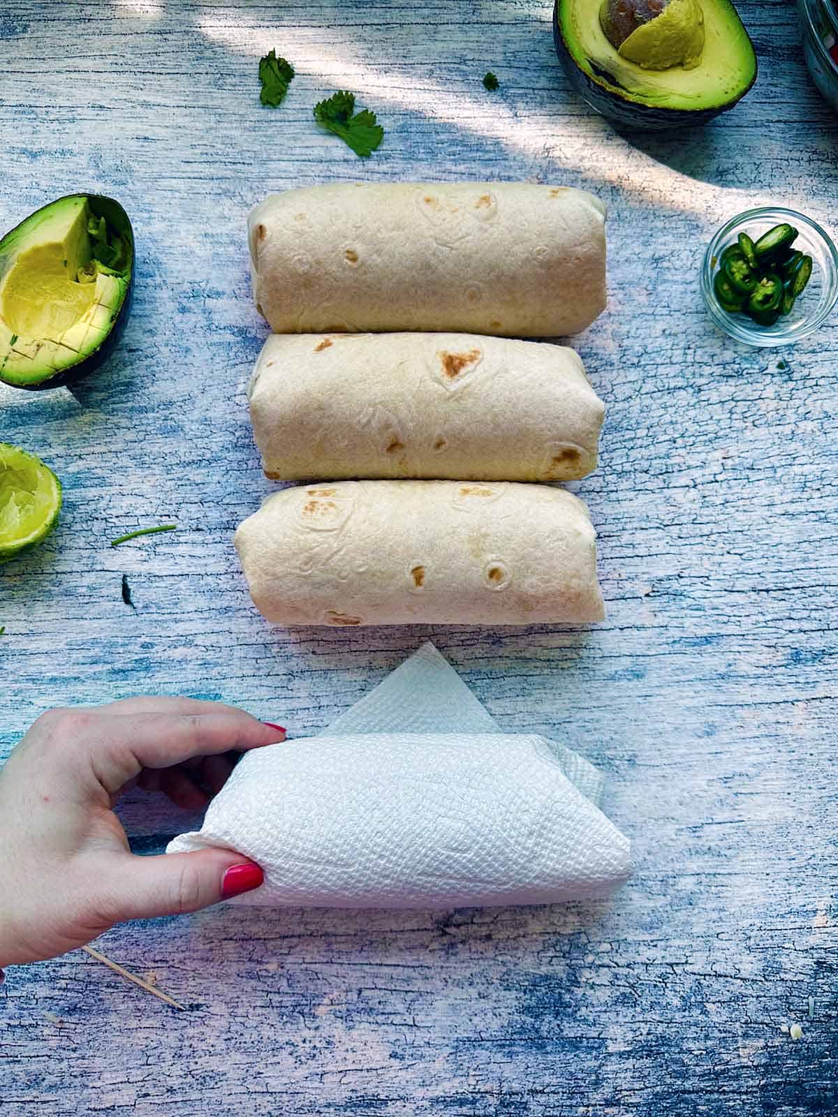 Make ahead burritos being wrapped in a paper towel to prepare for freezing and microwaving.