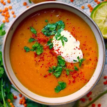 Square overhead photo of butternut squash red lentil soup with a dollop of yogurt, chopped cilantro, and red pepper flakes in a gray bowl.