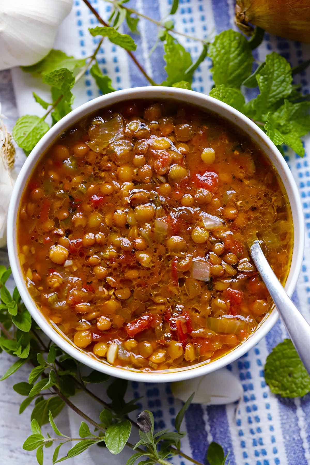 A close up photo of Greek Lentil Soup with buttered bread and a spoon in the bowl.