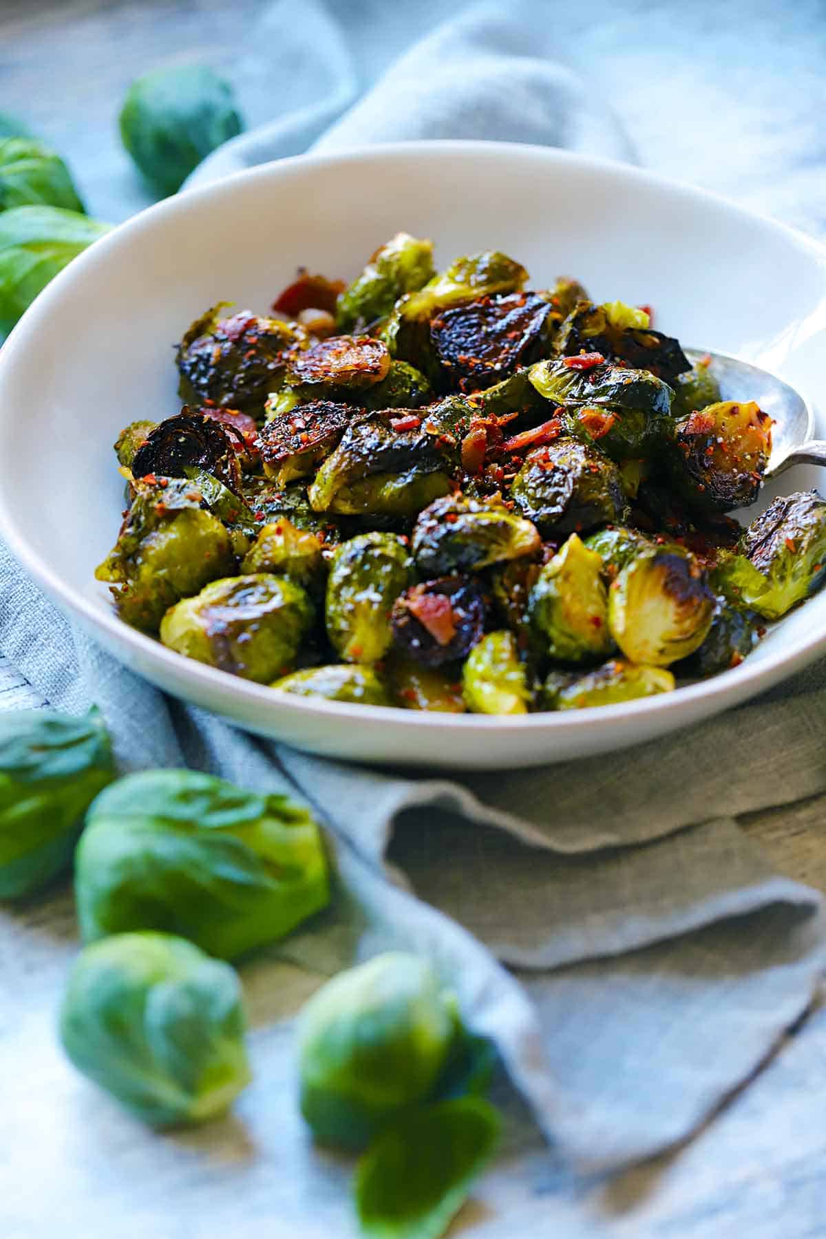 Side view of maple roasted brussels sprouts with raw brussels sprouts scattered around.