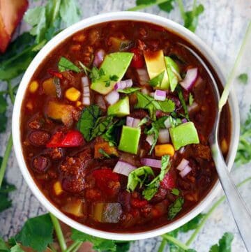 Overhead square photo of a pot of turkey chili with veggies and black beans with a wooden spoon.