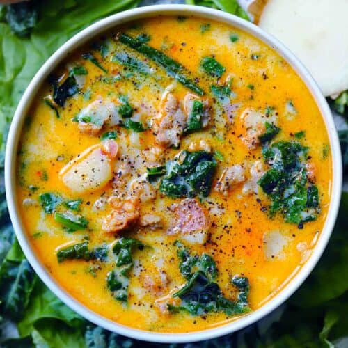 Square overhead photo of zuppa toscana with sausage, potatoes, and kale in a creamy broth, in a white bowl on a bed of greens.
