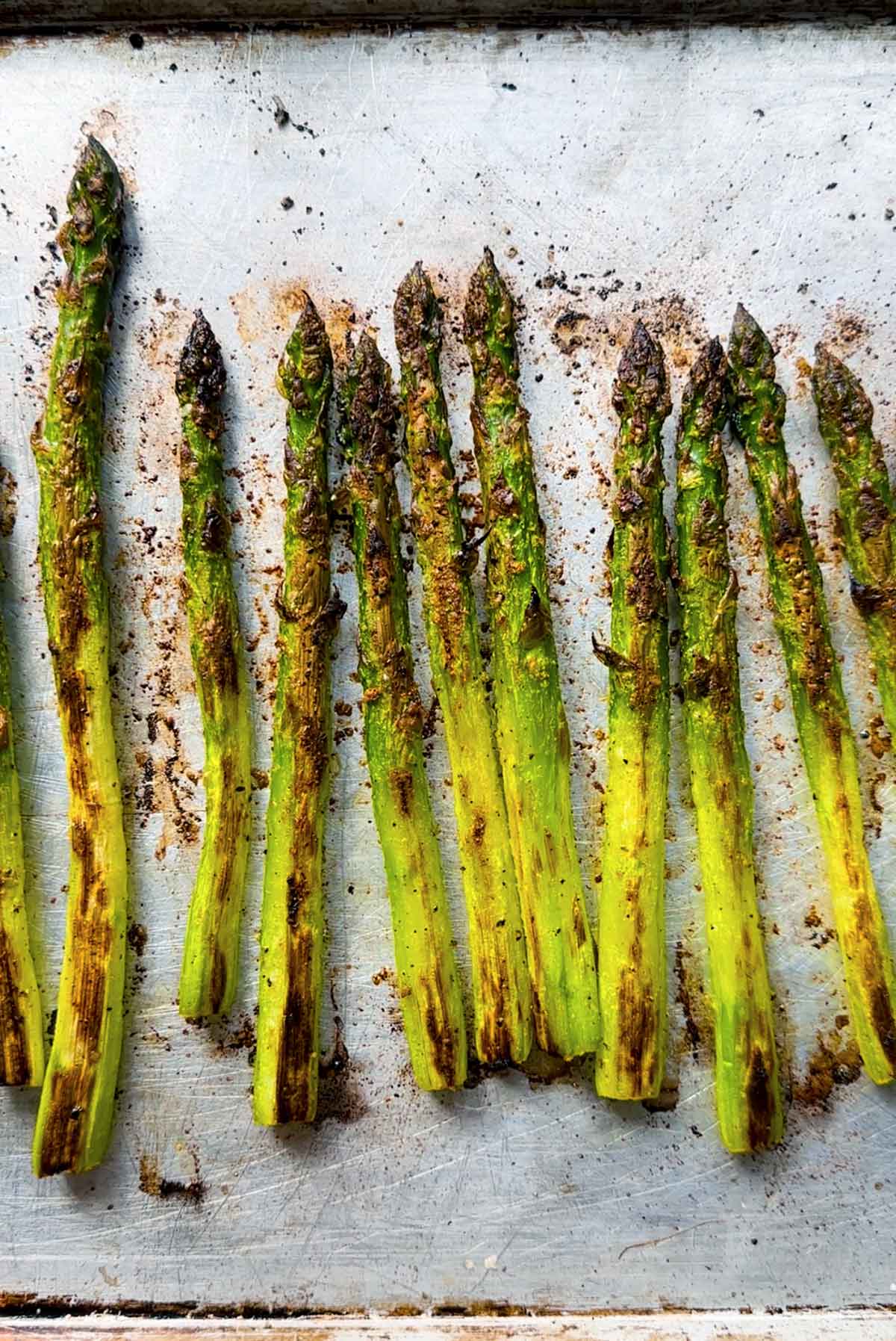 Roasted asparagus spears on a baking sheet showing how crispy the tips are and the browning from roasting.