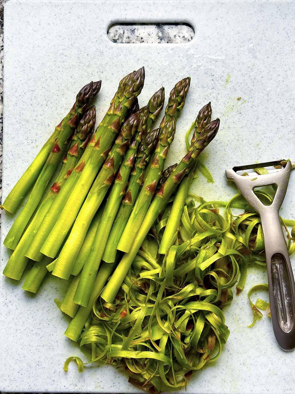 Asparagus that has been peeled on the bottom half, with peelings and the Y-peeler next to them.
