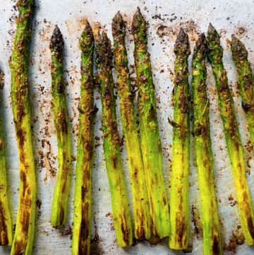 Square photo of Roasted asparagus spears on a baking sheet showing how crispy the tips are and the browning from roasting.