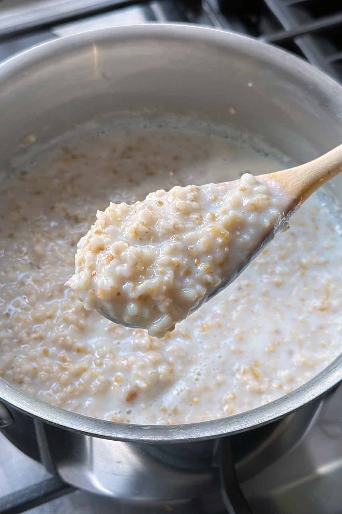 A wooden spoon with overnight steel cut oats on it lifting it out of the pot showing a close up of the texture.