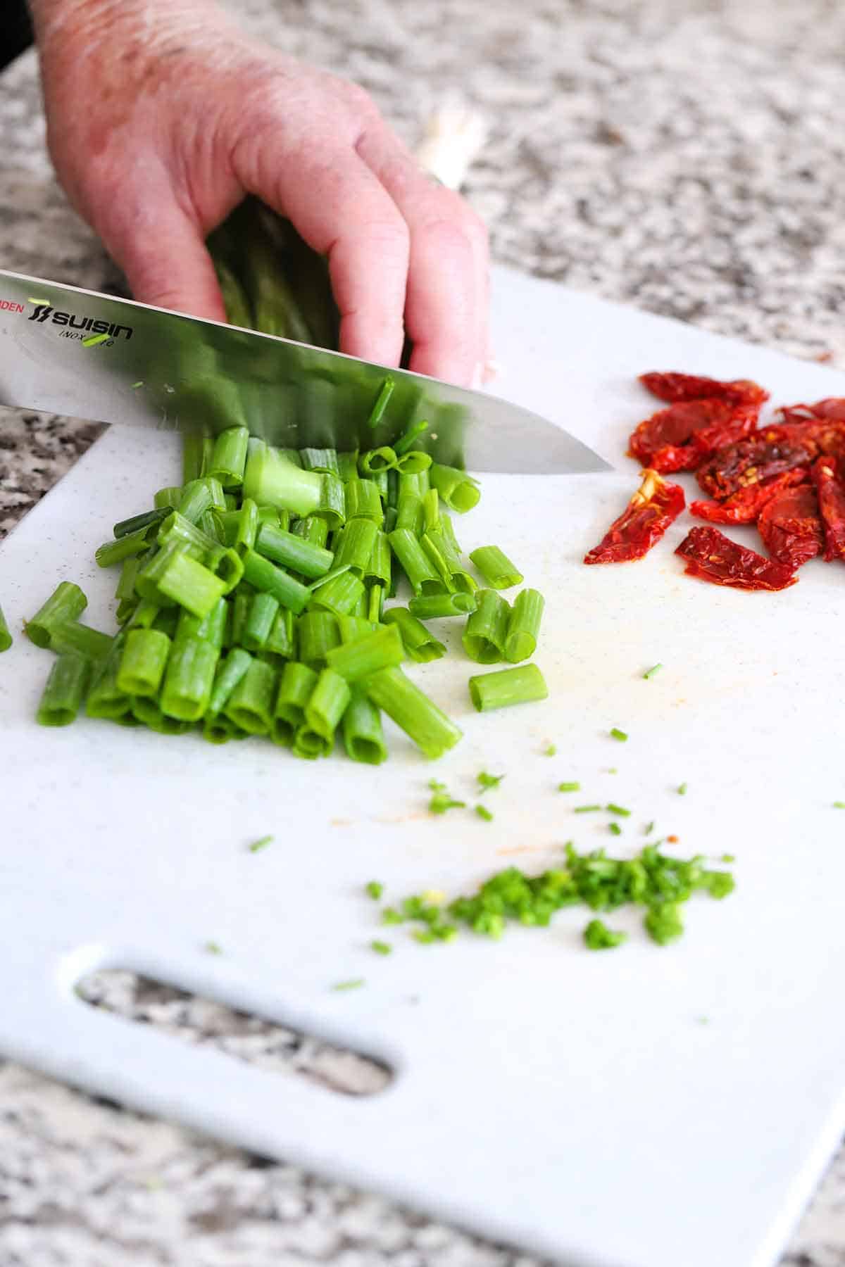 Image shows someone chopping green onions on a cutting board.