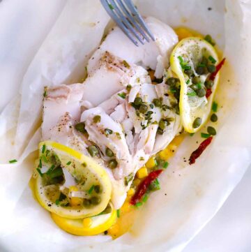 Square photo of fish en papillote, showing texture of cod fish flaked apart with a fork.