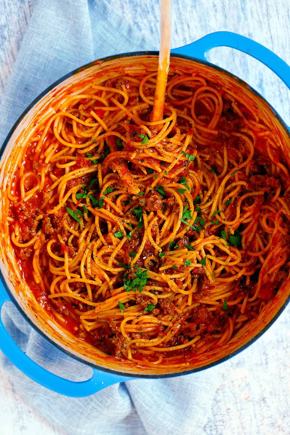 Top view of a pot with spaghetti and meat sauce garnished with parsley in a blue Dutch oven.