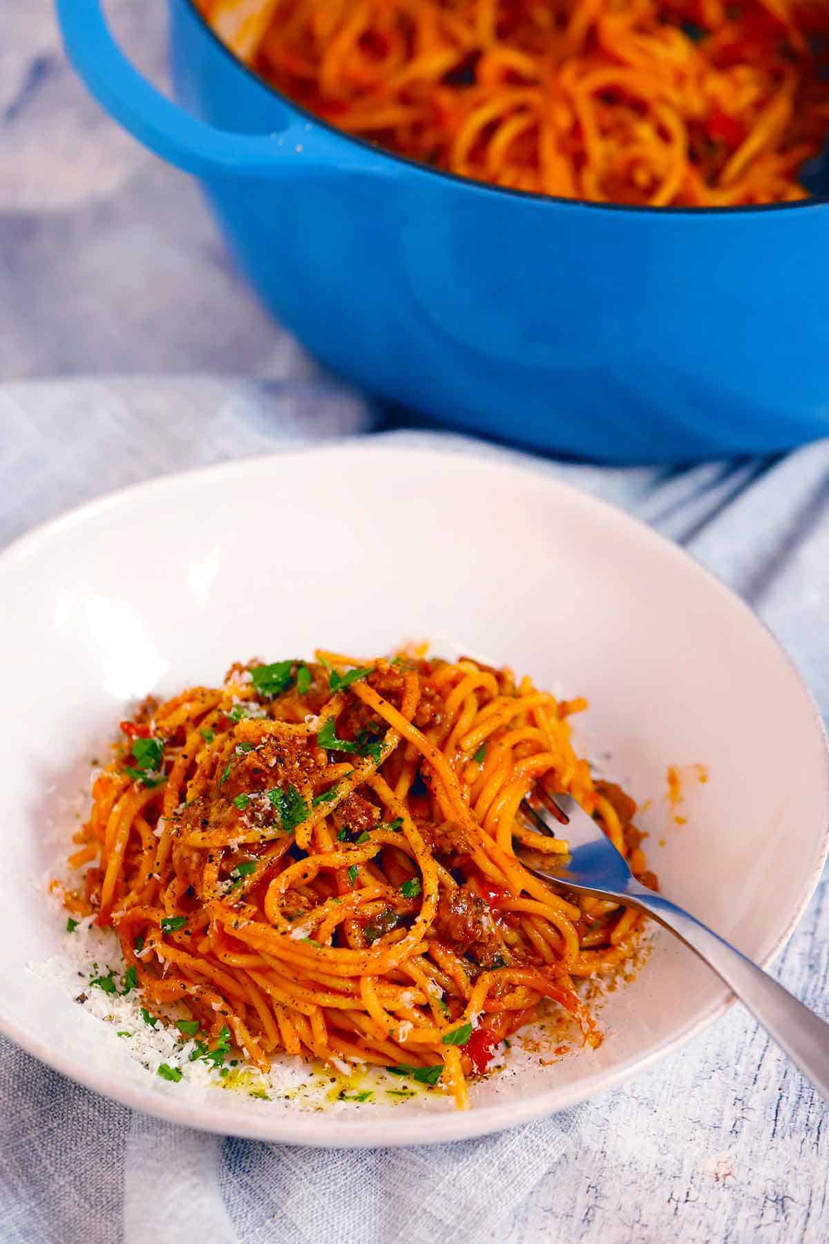 A plate of spaghetti and meat sauce in front of a blue dutch oven that has the rest of the one pot pasta recipe in it.