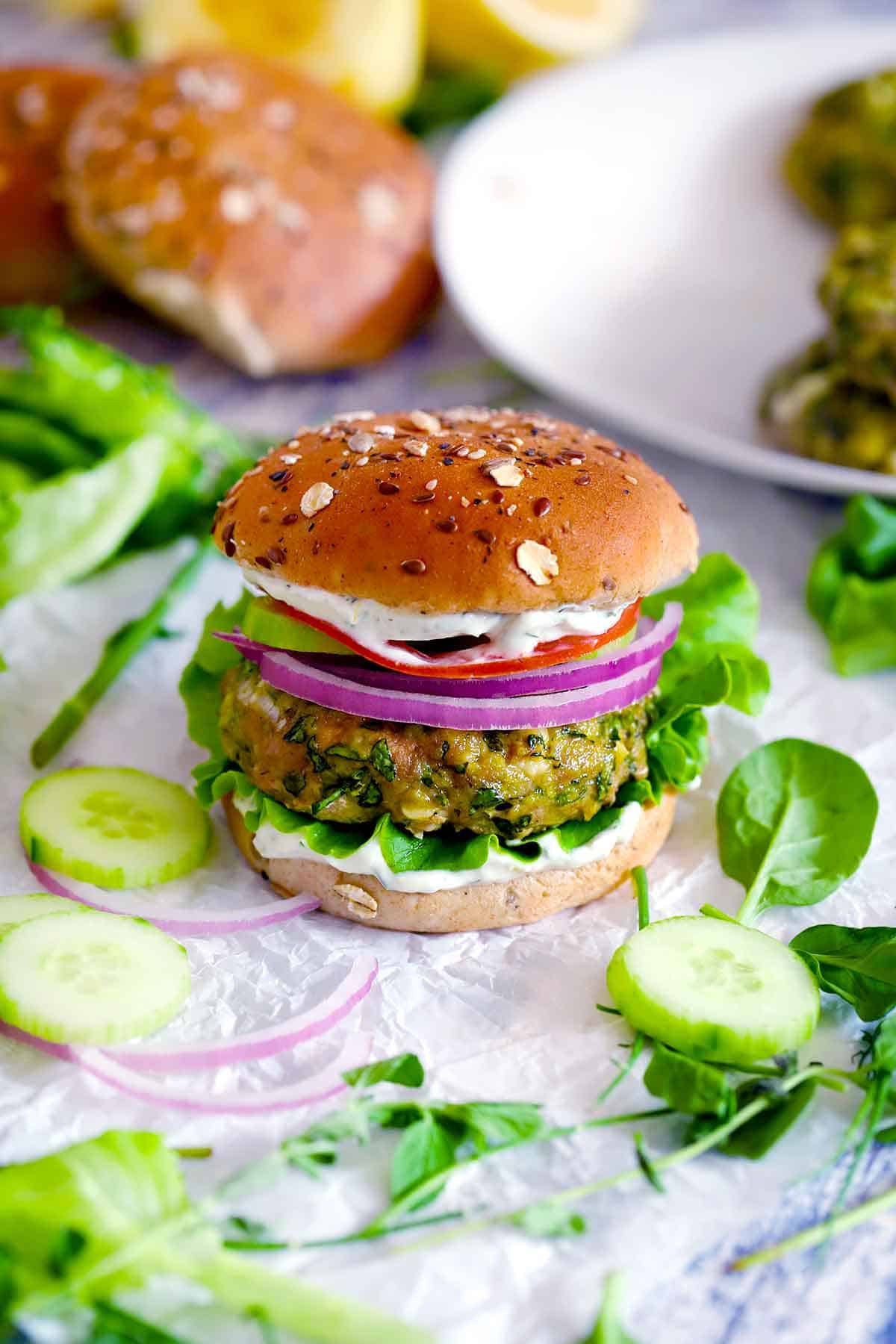 A spanakopita turkey burger, assembled, with ingredients scattered around it.