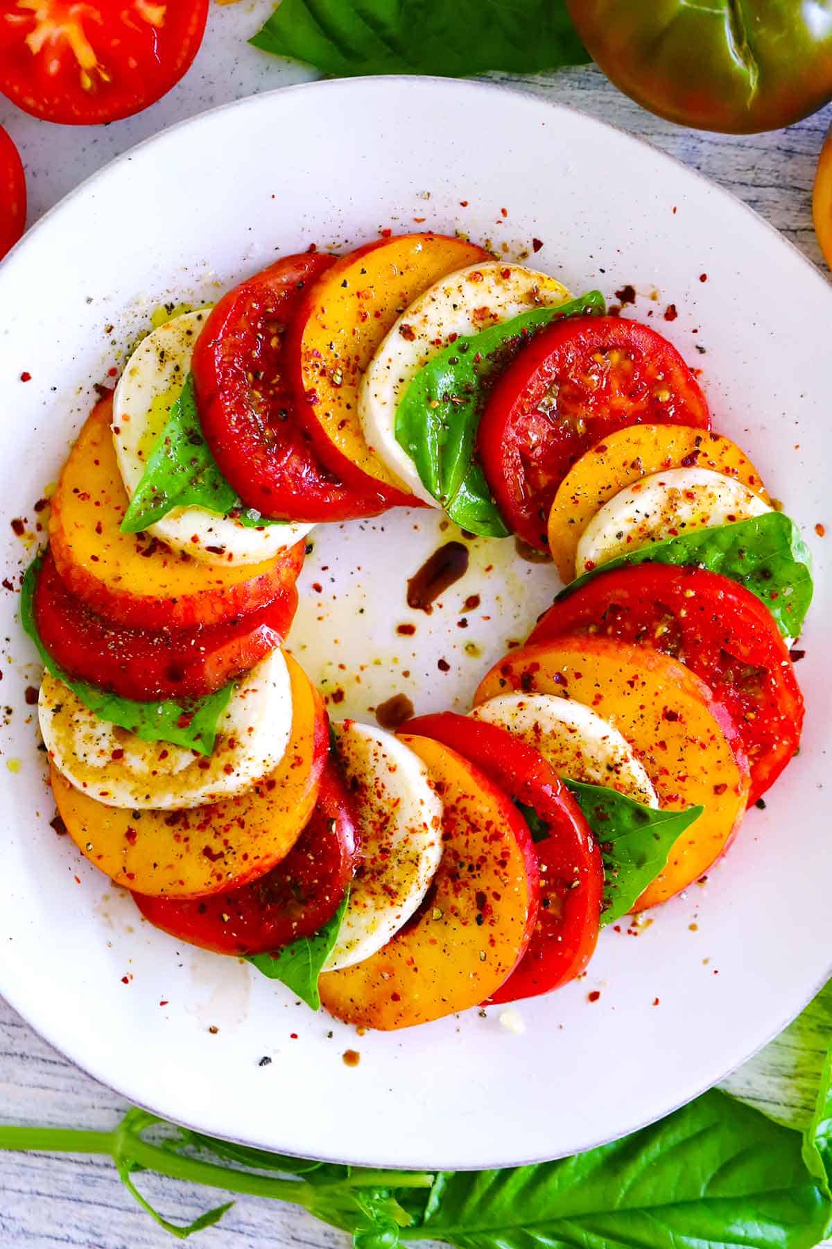 Overhead photo of a peach caprese salad on a white plate with ingredients arranged in a circular shape overlapping one another.