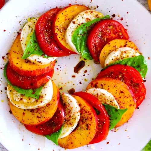 Square photo of peach caprese salad with ingredients layered in a circle overlapping one another on a white plate.