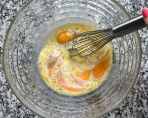 Whisking eggs, milk, olive oil, salt, and pepper in a large bowl.