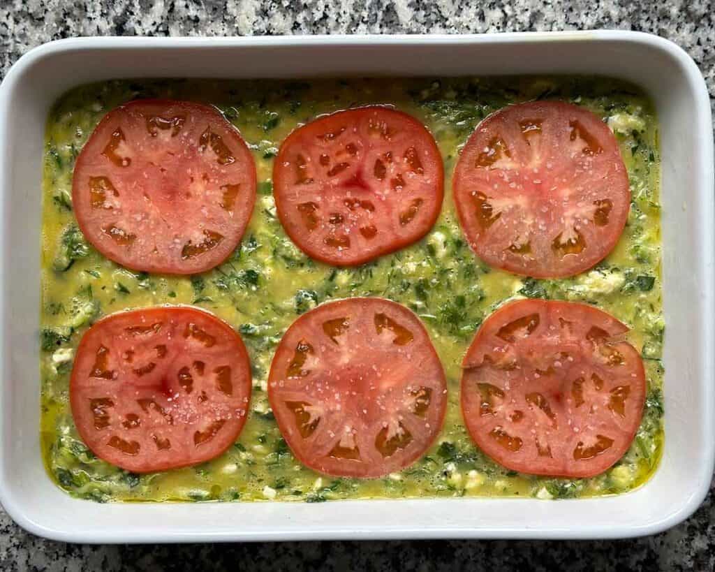 Greek zucchini casserole (sfougato) in a baking dish topped with tomatoes ready to be put into the oven to bake.