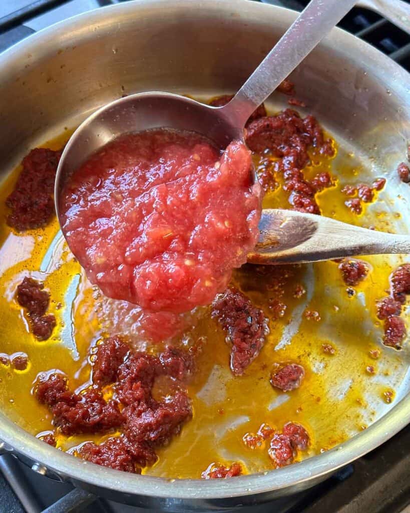 A ladle of tomato pulp being added into a skillet to make tomato sauce.