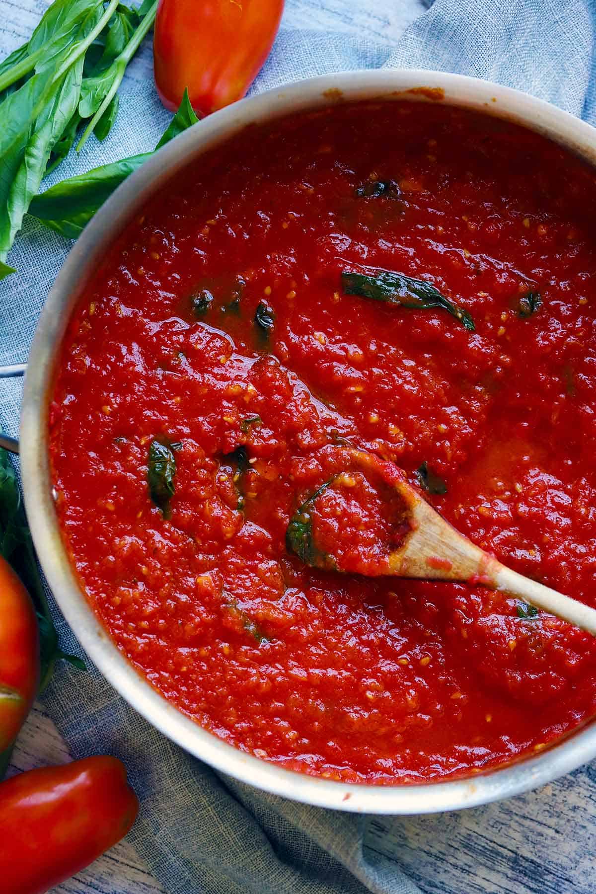 Overhead photo of a skillet full of tomato sauce made from scratch and a wooden spoon scooping it.