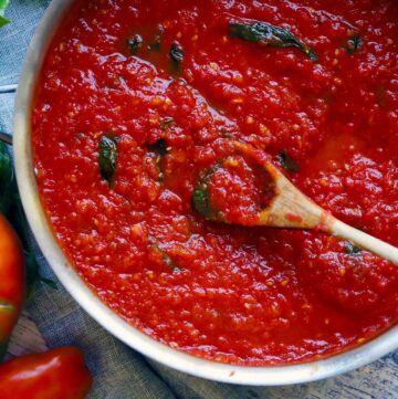 Square photo of overhead photo of fresh tomato sauce with basil, and a wooden spoon stirring it.