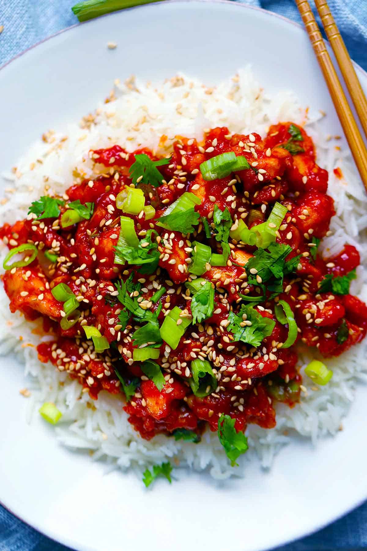 Overhead photo of gochujang tofu over rice with green onions and cilantro on top and chopsticks on the side.