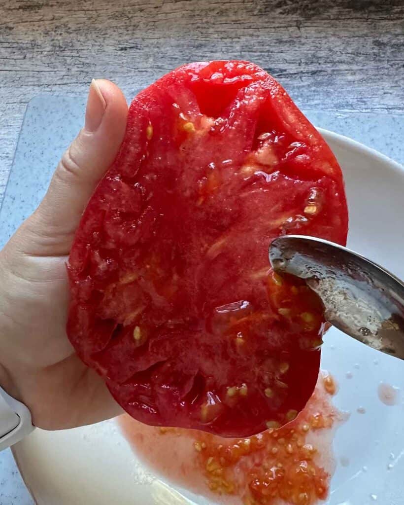 Using a spoon to help remove seeds from a tomato half.