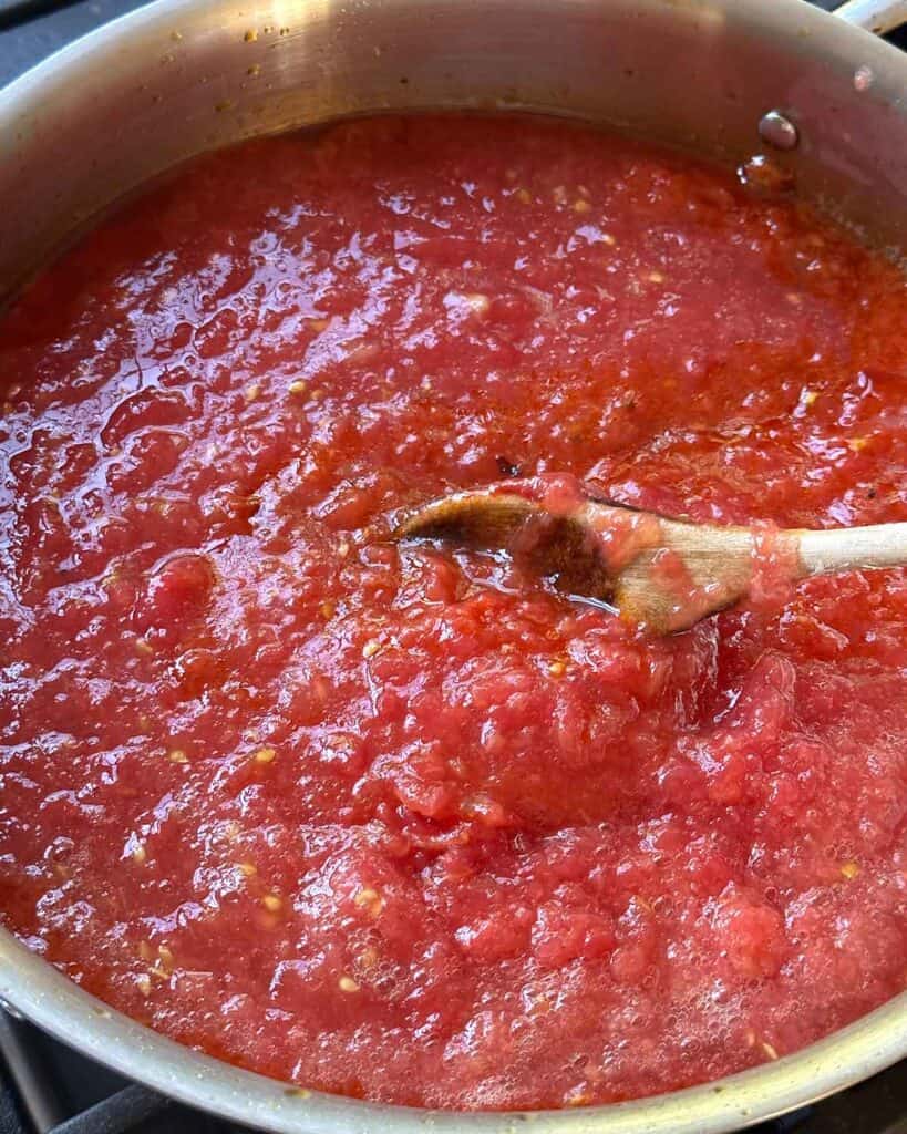 A wooden spoon stirring tomato sauce.