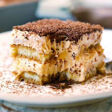 Square photo of a slice of pumpkin chai tiramisu taken from the side showing the layers and a bite taken out with a fork.