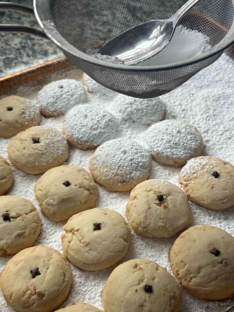 Dusting the tops of warm baked kourabiedes with sifted powdered sugar.