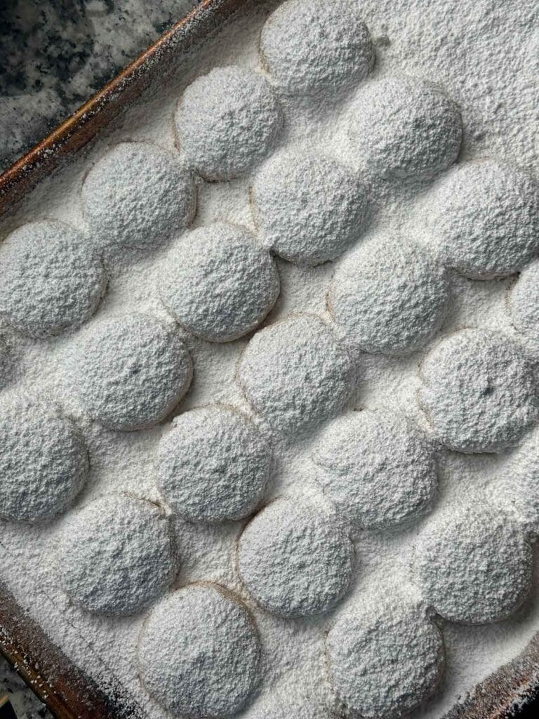 Cookie sheet full of powdered sugar coated kourabiedes.