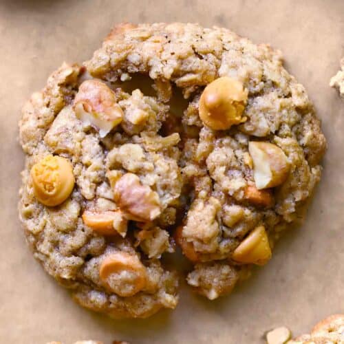 Close up overhead photo of an oatmeal butterscotch cookie with walnuts broken in half to show texture on brown parchment paper.