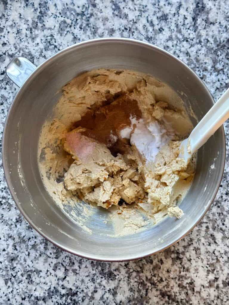 A mixing bowl showing cinnamon, salt, baking soda, and vanilla being added to cookie dough.