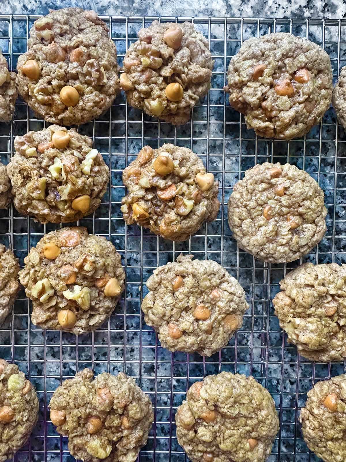 Oatmeal butterscotch cookies on a cooling rack, showing the difference in cookies with butterscotch chips and walnuts placed on top before baking verses baking them after scooping without anything added on top.