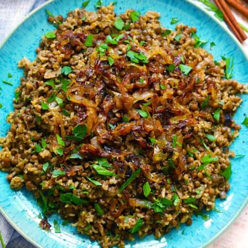 Square cropped overhead photo of Mujadara (lentils, rice, and caramelized onions) on a blue plate garnished with parsley.