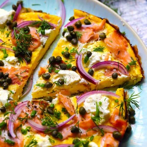 Square photo of an open faced omelette slice topped with smoked salmon, cream cheese, capers, and red onions.