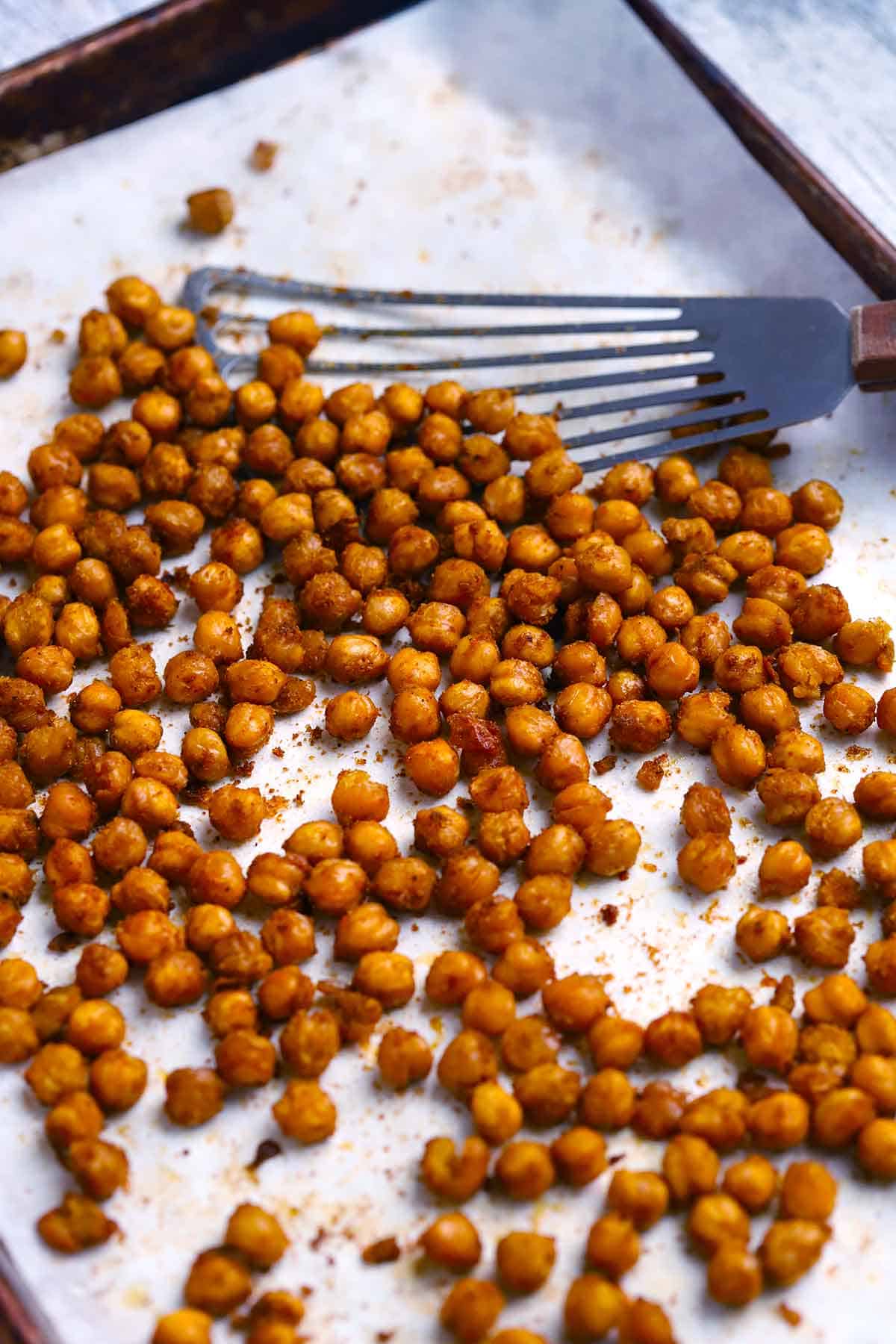 Roasted chickpeas on a sheet pan with a spatula scooping some up.