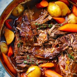 Square photo of Dutch Oven Pot Roast with Carrots and potatoes, garnished with thyme sprigs.