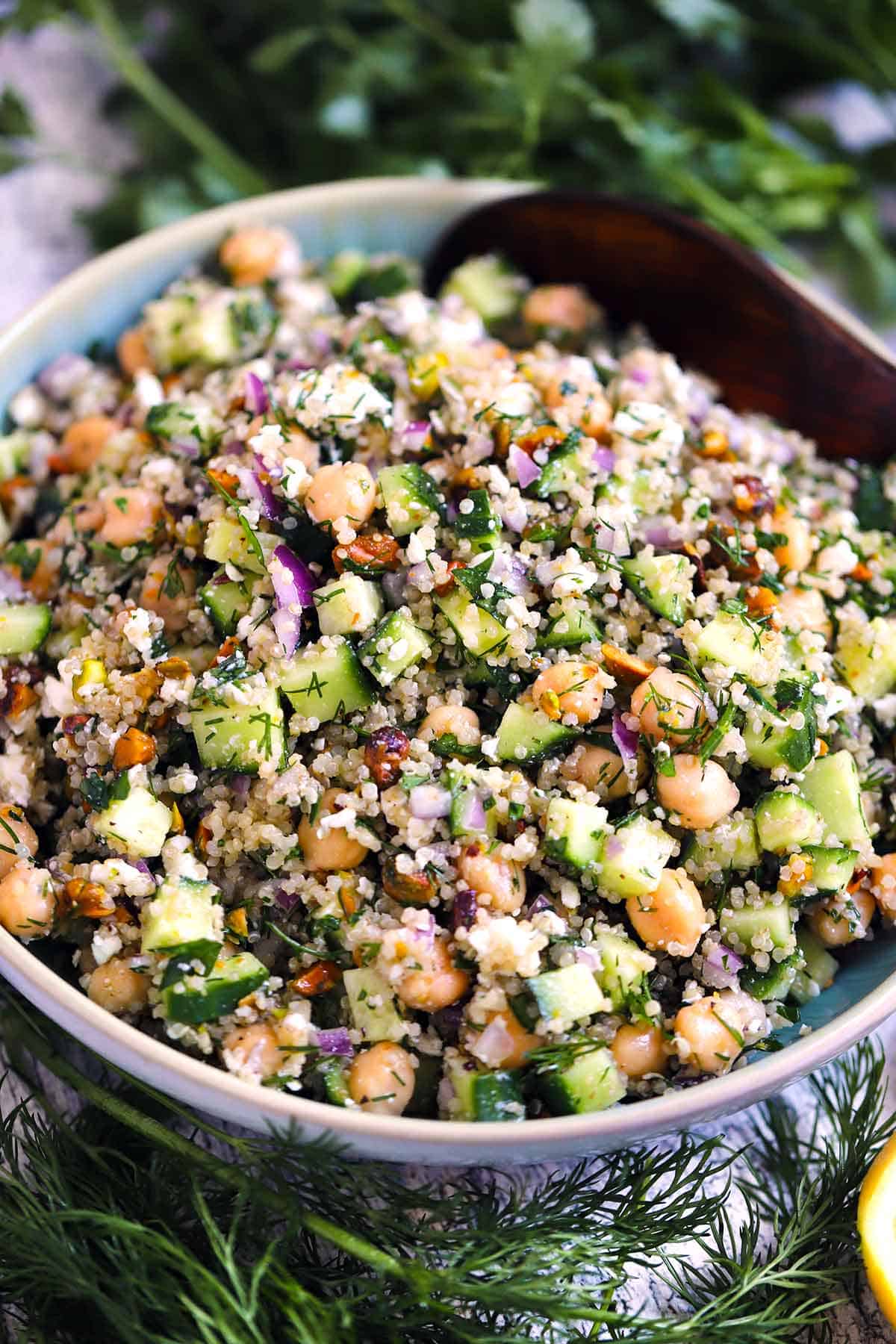 Close up view of the Jennifer Aniston Salad in a bowl with a wooden spoon and herbs scattered around.