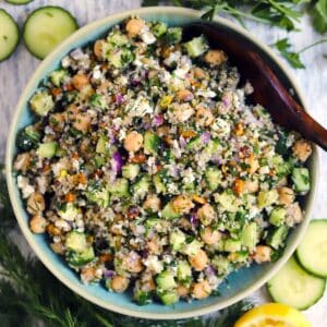 Square photo of an overhead shot of the Jennifer Aniston Salad in a blue bowl with a wooden spoon in it and ingredients scattered around.