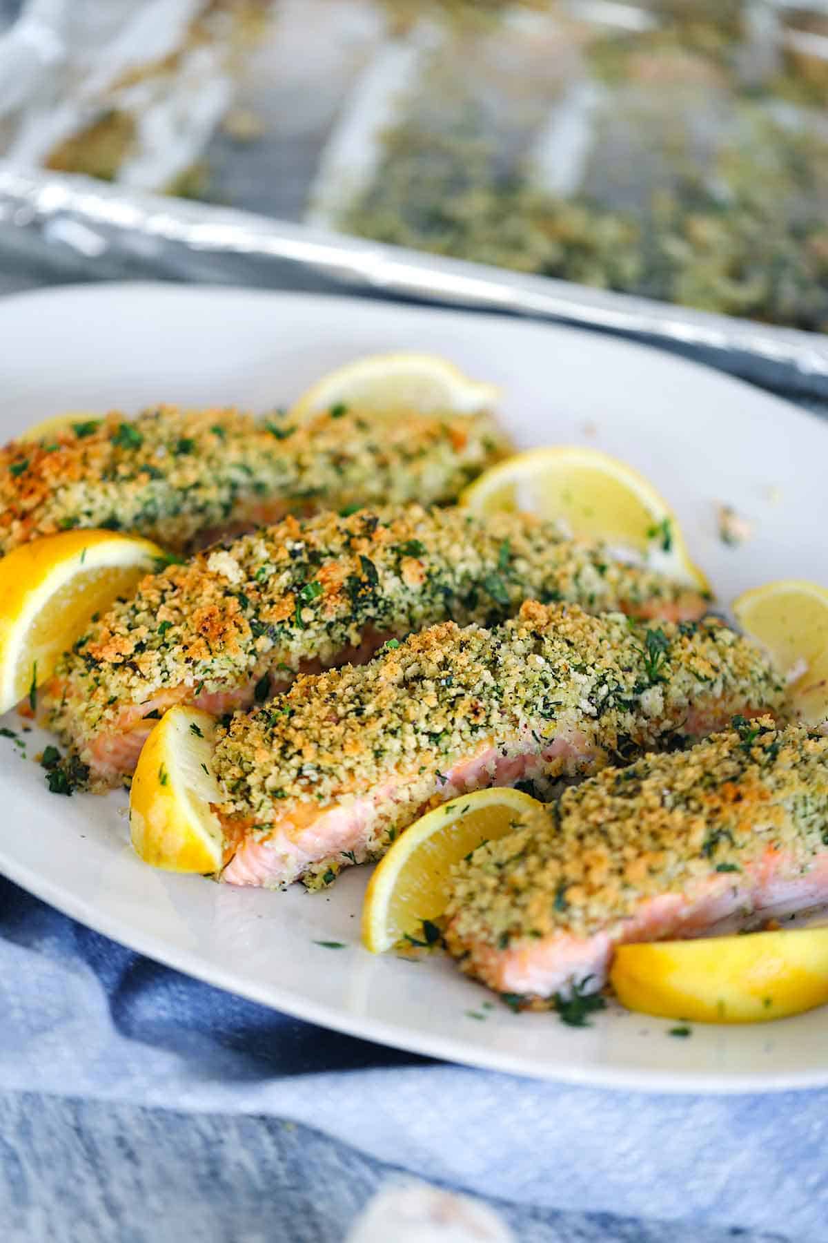 A platter of four filets of panko crusted salmon with lemon wedges around it.