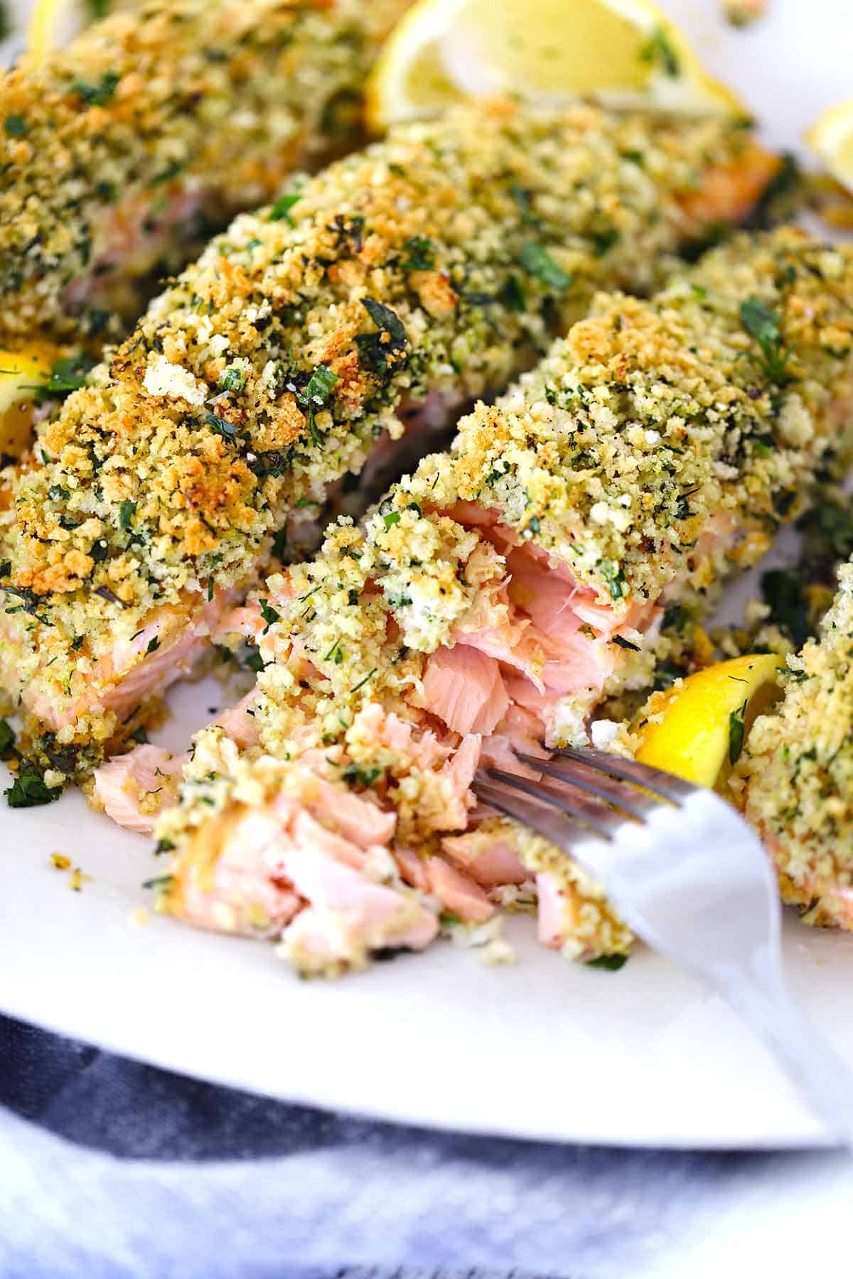 A fork flaking apart a filet of panko crusted salmon, showing the flaky and moist texture inside.