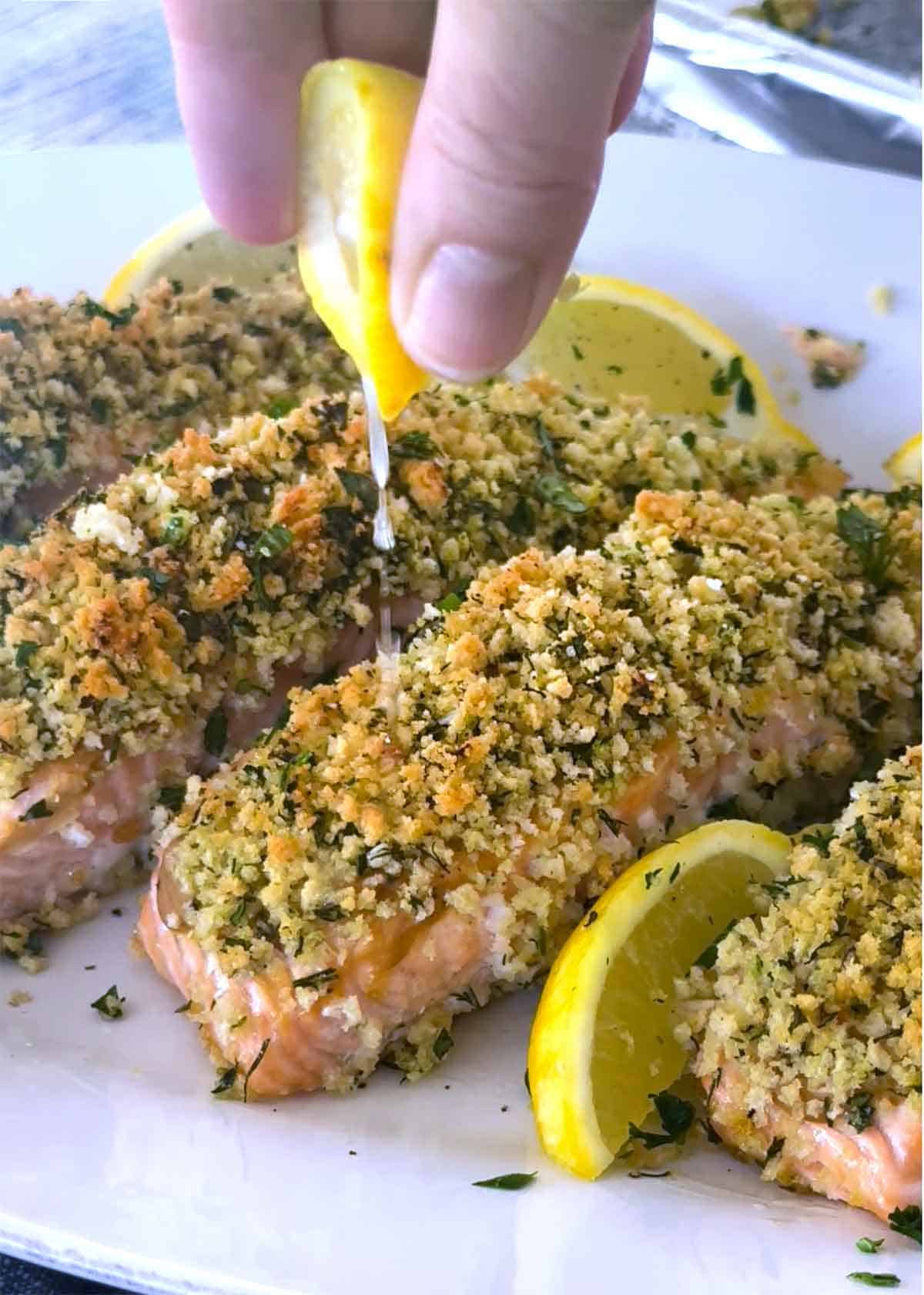 Someone squeezing a lemon on top of a filet of panko crusted salmon.