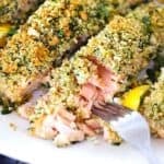 Square photo of a fork flaking apart panko crusted salmon, showing the texture, on a plate.