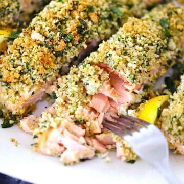 Square photo of a fork flaking apart panko crusted salmon, showing the texture, on a plate.