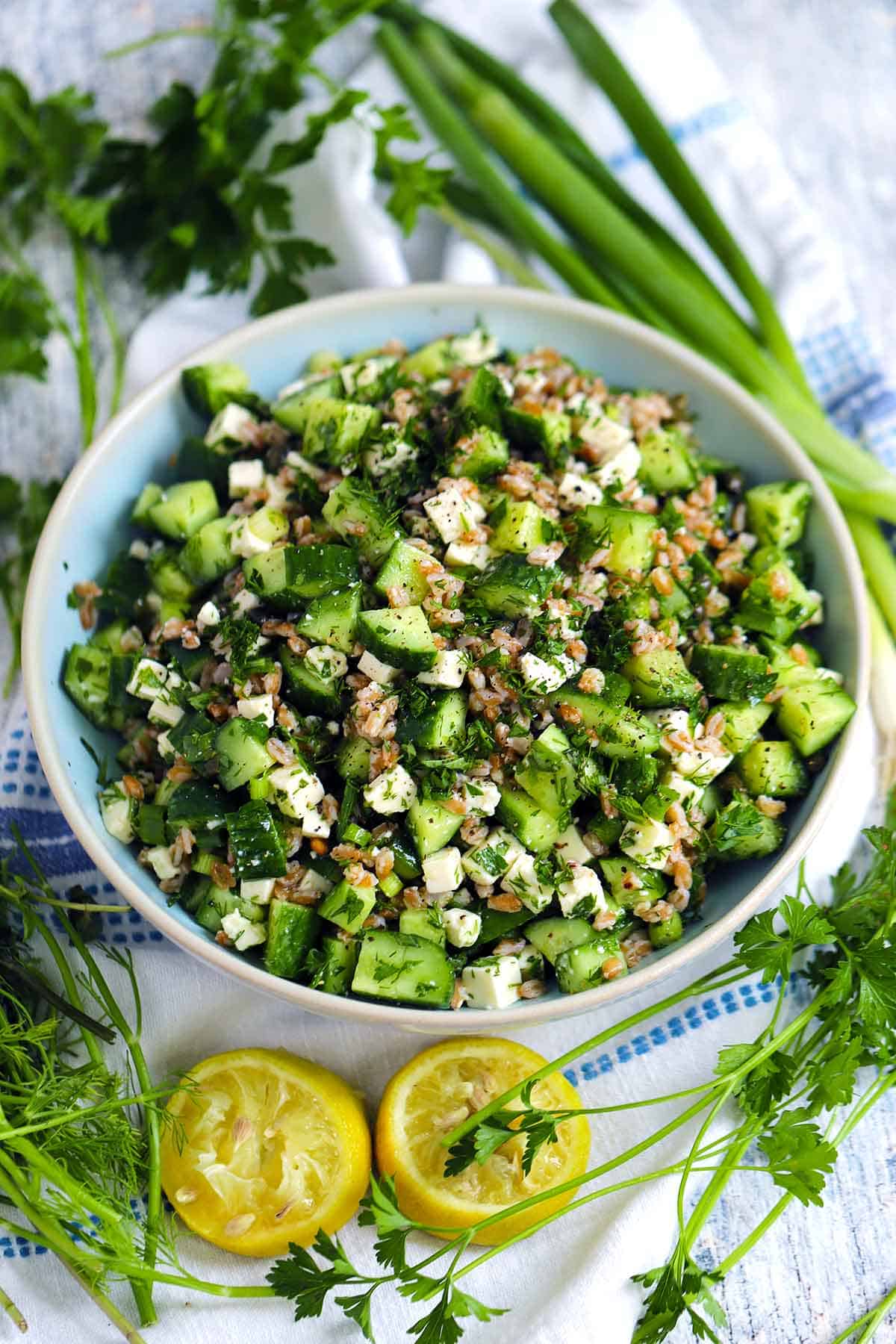 A bowl of farro salad with lemons, green onions, and herbs scattered around.