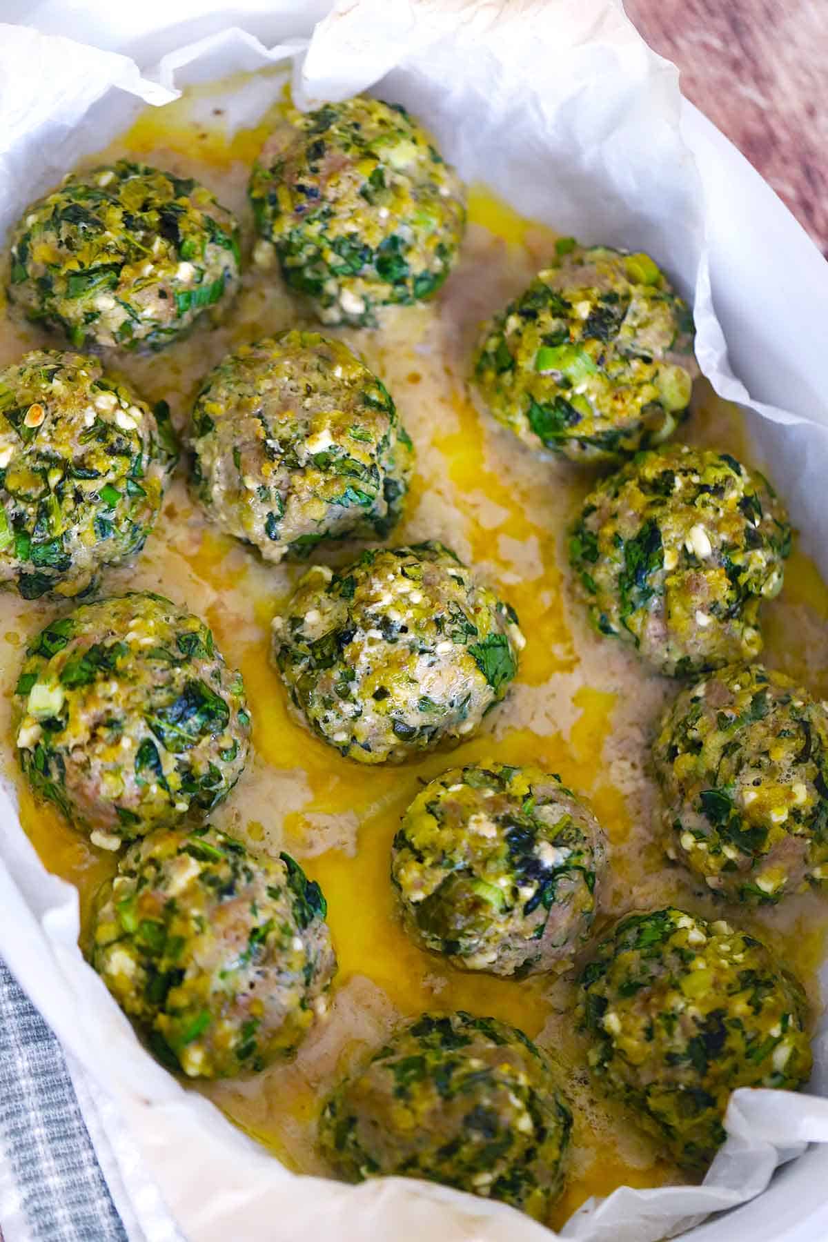 Overhead view of baked spanakopita turkey meatballs with lemon butter in a baking dish lined with parchment.